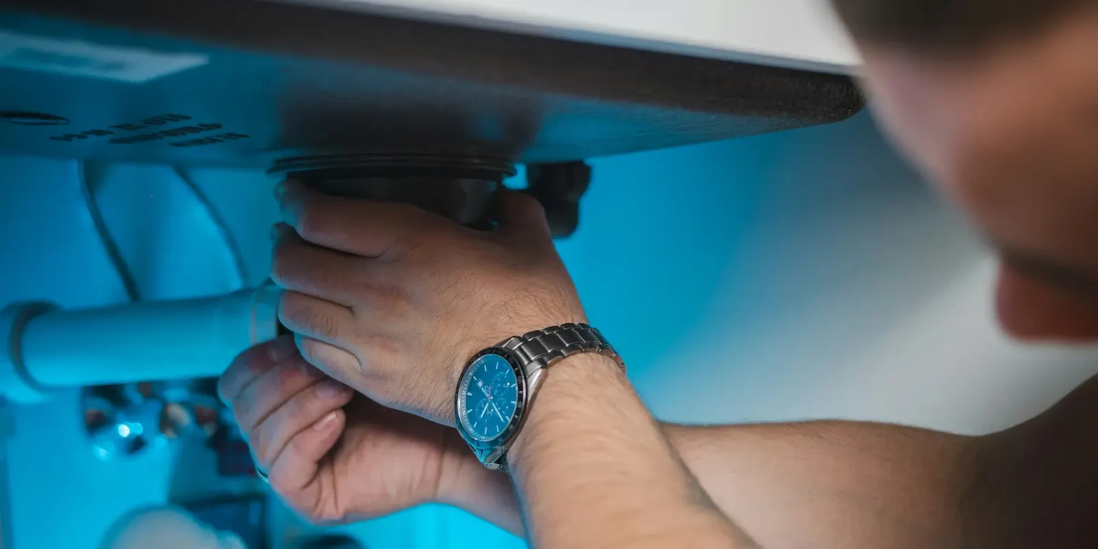 Technician installing a filter housing under a sink lit by blue light